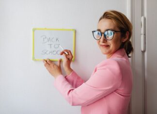 Nauczycielka w różowej marynarce pisze na tablicy Back to School