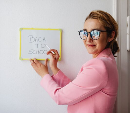 Nauczycielka w różowej marynarce pisze na tablicy Back to School