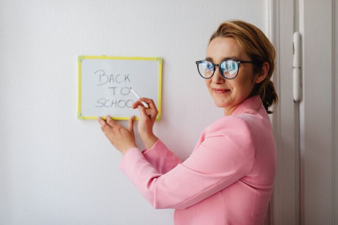 Nauczycielka w różowej marynarce pisze na tablicy Back to School